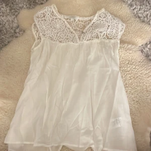 Vit topp med spetsdetaljer - Säljer en söt vit topp med vackra spetsdetaljer upptill. Klänningen har en luftig passform och är perfekt för varma dagar. Den är ärmlös. Perfekt för en somrig look! 🌸