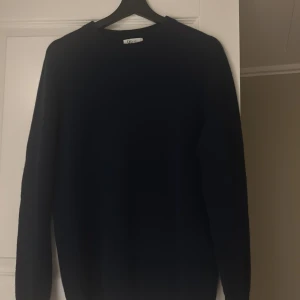 Mörkblå tröja  - Säljer en stilren mörkblå tröja,Tröjan har en klassisk design med långa ärmar och rund hals. Perfekt för en minimalistisk garderob. Tröjan är helt oanvänd och lappar och påse ingår. Nypris är 849. 