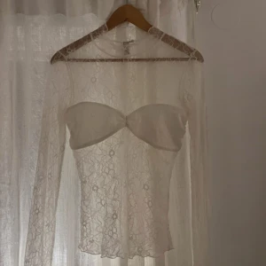Vit spetsblus med långa ärmar - Säljer en elegant vit spetsblus med långa ärmar. . Blusen är genomskinlig och har en tight passform. Se bild på hål. 