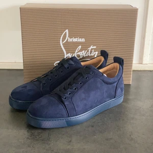 Blå sneakers från Christian Louboutin - Snygga mörkblå sneakers från Christian Louboutin i mocka med den ikoniska röda sulan. Skorna har snörning och en stilren design som passar perfekt för en trendig look. Levereras med originalförpackning och dustbag. Finns inte din storlek? Vi kan fixa alla storlekar bara att höra av sig så löser vi de du vill ha! Vi kan även fixa alla skor, tröjor, jackor, västar osv till riktigt bra pris bara att skicka bild på vad du söker och storlek så ska vi göra de vi kan!/// Es Clothing