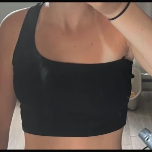 Svart oneshoulder topp - Snygg svart oneshoulder topp med en stilren design. Perfekt för en trendig look. Passar bra till både jeans och kjol.