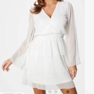 Vit studentklänning  - Snygg vit omlottklänning med v-ringning och långa ärmar. Klänningen har volanger och en elastisk midja för en bekväm passform. Perfekt för studentklänning eller andra tillfällen. Aldrig använd💕💕🙌🏻🙌🏻