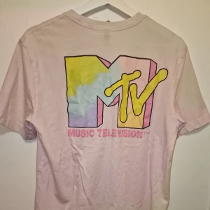 Rosa MTV t-shirt - Säljer en rosa t-shirt med det ikoniska MTV-logotypen i pastellfärger på både fram- och baksidan. Perfekt för dig som älskar retro och musik! 🎶