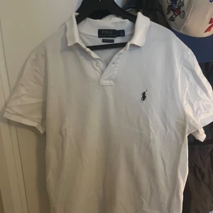 Vit pikétröja från Ralph Lauren - Säljer en klassisk vit pikétröja från Ralph Lauren i custom slim fit. Tröjan har korta ärmar och den ikoniska broderade loggan på bröstet. Perfekt för en stilren look.