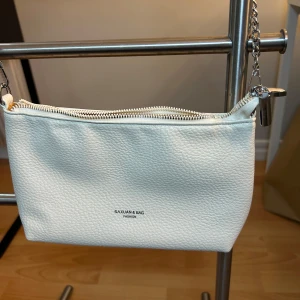 Vit axelväska från Shein  - Stilren vit axelväska i skinnimitation från Shein. Väskan har en silverfärgad kedjerem, dragkedja upptill och ett ljust innerfoder med extra innerficka. Perfekt storlek för det viktigaste och passar till många outfits.