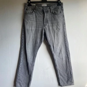 Grå raka jeans från Jack & Jones - Snygga grå jeans från Jack & Jones i klassisk rak modell. Jeansen har fem fickor, bälteshällor och stängs med dragkedja och knapp. Perfekta till en avslappnad streetstil och funkar året runt.