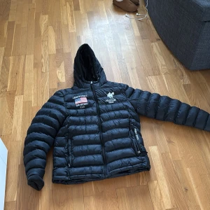 Svart pufferjacka från Polo Club Vinson - Säljer en svart pufferjacka med huva från Polo Club Vinson. Jackan har broderade detaljer på bröstet, dragkedja framtill och två fickor med dragkedja. Perfekt för kyliga dagar och riktigt skön att ha på sig.