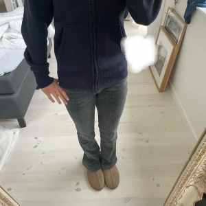Mörkgrå lågmidjade bootcut jeans - Säljer ett par mörkgrå lågmidjade bootcut jeans med klassisk femficksdesign och normal passform. Jeansen har en snygg tvättad look och är tillverkade i mjukt bomullsmaterial med lite stretch för extra komfort. Perfekta för dig som gillar en avslappnad men ändå trendig stil. Säljer då de tyvärr inte kommer till användning. Pris kan diskuteras