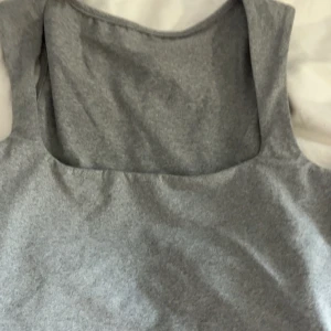 Grå ärmlös linnetopp XS - En stilren grå ärmlös linnetopp med fyrkantig ringning. Toppen är i mjukt och stretchigt material som sitter snyggt på kroppen. Perfekt att matcha med jeans eller kjol för en clean look.