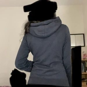 Mörkblå zip-hoodie från Hollister - Mörkblå hoodie från Hollister med dragkedja och huva. Stora vita bokstäver framtill och snörning i huvan. Mjuk bomullskänsla och normal passform, perfekt för chill dagar. Klassisk streetstil med långa ärmar och fickor framtill.