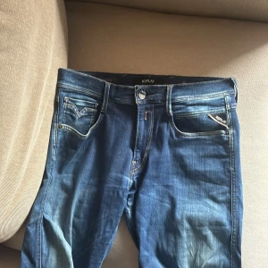 Blå jeans från Replay - Snygga blå jeans från Replay med klassisk femficksdesign och ljusa slitningar. Jeansen har raka ben, normal passform och detaljerade sömmar på bakfickorna. Tillverkade i mjukt jeanstyg med en cool tvättad look och läderpatch bak i midjan.