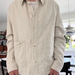 Beige overshirt med knappar - Stilren beige overshirt  med klassisk krage och stora framfickor. Jackan har knäppning framtill med fyra knappar och är tillverkad i ett grovt bomullstyg. Perfekt för lager-på-lager och enkel att matcha. Använd 1 gång