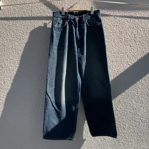Weekday Astro Loose Baggy Jeans - Säljer ett par blå Weekday Astro Loose Baggy Jeans med knappar i gylfen och klassiska fem fickor. Jeansen har en lös och baggy passform med raka, vida ben och är tillverkade i denim. Storlek W28/L32. Knappt använda.