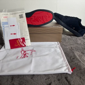 Mörkblå sneakers från Christian Louboutin - Säljer ett par mörkblå sneakers från Christian Louboutin i mocka med klassisk röd sula. Skorna har snörning, rund tå och diskret broderad logga på hälen. Innersulan är ljusbrun och märkt med Louboutin-loggan.