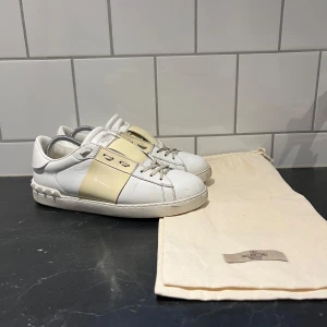 Valentino Open sneakers med beige detalj - Säljer ett par Valentino Open med en krämvit unik design. Skorna har snörning och rund tå, tillverkade i skinn.                                                                    Dem är autentiska, äkthetscertifikat finns! 
