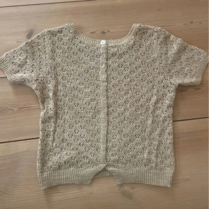 Beige stickad kortärmad kofta  - Säljer en beige stickad kofta från Skovhuus i storlek M. Tröjan har korta ärmar, rund halsringning och fina knappar baktill. Mönstret är hålstickat💕💕
