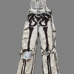 Grå denim hängselbyxor med svart skelettmönster - Hemgjorda hängselbyxor som jag haft ett tag. De går att tvätta med vanlig tvätt. Tirktymmla. Stryka och allt sånt där. Andvänder dom inte längre pga att de fastnar i min navelpircing då de inte är lågmidjade på mig. (90 cm höft ish). Tycker de e tråkigt att slänga så aa. Som är vida på passformen