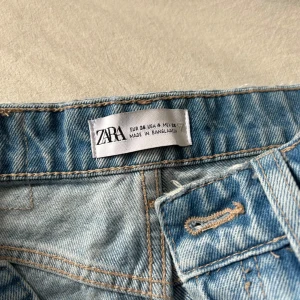 Ljusblå ripped jeans från Zara - Ljusblå jeans från Zara i klassisk denim med raka ben och stora slitningar över knäna. Byxorna har hög midja, knappgylf och femficksmodell. Perfekta för en avslappnad och trendig look. Använda 2 gånger💕