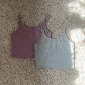 2-pack ribbade croppade linnen - Säljer två croppade linnen med smala axelband, ett i ljuslila och ett i ljusblått. Båda är ribbade och har en enkel, stilren design som passar perfekt till jeans eller kjol. Materialet är mjukt och stretchigt, vilket gör dem riktigt sköna att bära. Säljs tillsammans för 40 kr annars 25 kr styck.