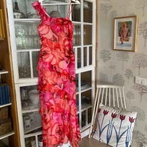 Rosa/röd volangklänning Boohoo - Magisk slutsåld långklänning från Boohoo med blommigt mönster i rosa och rött. Perfekt till midsommar!! Klänningen har volanger och asymmetrisk axel med smala axelband. Har ingen bild på mig då den är lite tight för mig som vanligtvis är en st 38. Den följer ens kurvor!