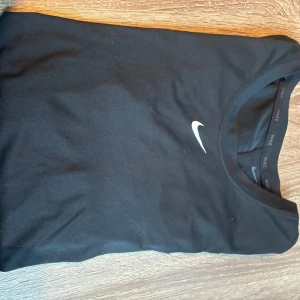 Svart långärmad träningströja Nike - Svart långärmad träningströja från Nike med klassisk vit swoosh-logga på bröstet. Tröjan har rund halsringning och är tillverkad i ett mjukt, stretchigt material som andas. Perfekt för gymmet eller löprundan.