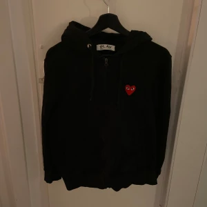 Svart zip hoodie från Comme des Garçons Play - Hej, jag säljer svart hoodie från Comme des Garçons med det ikoniska röda hjärta broderat på bröstet. Hoodien är väldigt bekväm och i toppskick då den inte har nå defekter eller fläckar. Pris kan diskuteras! 