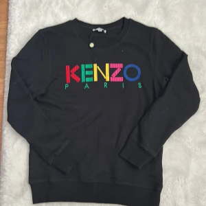 Svart Kenzo sweatshirt med färgglatt tryck - Svart sweatshirt från Kenzo med färgglatt broderat logotyptryck på bröstet. Tröjan har rund hals, långa ärmar och är tillverkad i 100% bomull. Perfekt för dig som gillar streetstyle och vill sticka ut med en ikonisk look.