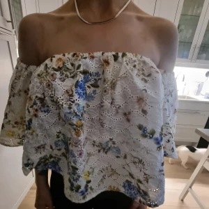 Blommig offshoulder blus från Zara Woman🌸 - Säljer en vit offshoulder blus från Zara Woman med broderade blommor i blått, grönt och gult. Blusen har vida ärmar och vackra spetsdetaljer i tyget. Perfekt för en somrig look med romantisk känsla.🌸🫶🏻