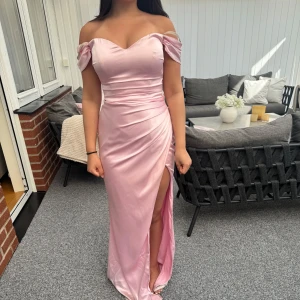 Ljusrosa långklänning från Dressroom Linne - Säljer en elegant ljusrosa långklänning från Dressroom Linne. Klänningen har offshoulder-modell, omlottdetaljer vid bysten och en hög slits framtill. Tillverkad i ett glansigt, mjukt material som ger en lyxig känsla. Klänningen är endast använd under en kväll. Köptes för 4000 kr och säljer för 2000. priset kan diskuteras vid snabb affär. 