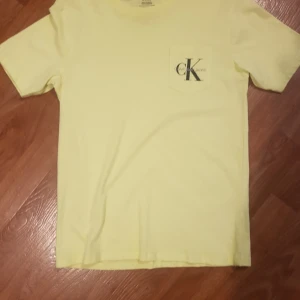 Gul t-shirt från Calvin Klein Jeans - Snygg gul t-shirt från Calvin Klein Jeans med klassisk CK-logga på bröstfickan. T-shirten är i mjuk bomull och har en enkel, stilren design med korta ärmar. Perfekt för dig som gillar minimalistisk stil och vill sticka ut med en fräsch färg.