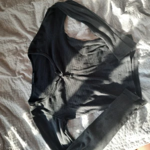 Svart ribbad långärmad topp - Svart långärmad topp med ribbad struktur och knappar vid halsringningen. Snygg och enkel modell med smickrande passform, perfekt att styla med jeans eller kjol. Mjuk och stretchig känsla.