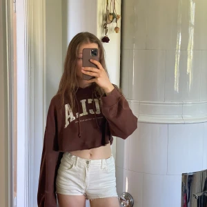 Brun croppad hoodie från Divided x UCLA -  brun croppad hoodie från h&m Divided med vit tryckt text framtill, huva och långa, lite bredare ärmar. Mjuk på innsidan och stor luva.