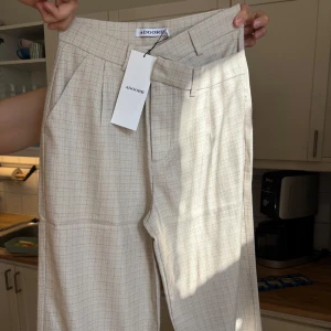 Beige rutiga kostymbyxor från ADOORE - Snygga beige kostymbyxor med rutmönster från ADOORE. Byxorna är aldrig använda och är helt nya. Nypris 1295 kr. Passar till varje tillfälle.