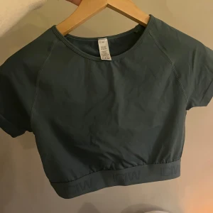 Grön kortärmad topp från ICANIWILL - Snygg grön kortärmad topp från ICANIWILL med elastisk kant nedtill. Perfekt för träning eller en avslappnad dag. Materialet är mjukt och stretchigt för bästa komfort.