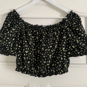 Svart blommig offshoulder topp - Säljer en söt svart offshoulder topp med små gula blommor. Toppen är croppad och har korta puffärmar med elastiska kanter. 