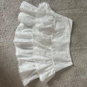 Vit volangkjol - Charmig vit kortkjol med volanger och broderade blommor. Perfekt för en somrig look med sin lätta och luftiga design.