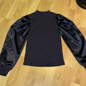 Blå tröja med satinärmar från Shein - Snygg blå tröja från Shein med unika satinärmar som ger en lyxig känsla. Tröjan har en ribbad hals och långa ärmar, perfekt för en stilren look. Passar bra till både jeans och kjol. Aldrig använd