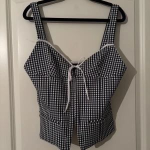 korsettopp från zara - Snygg svartvit rutig korsettopp med breda axelband och knytning framtill. Perfekt för en trendig look. Toppen har en figurnära passform och är gjord i ett bekvämt material. Storlek L men passar M:)