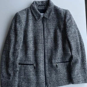 Rutig jacka från Basler - Snygg rutig jacka från Basler med dragkedja framtill. Jackan har en klassisk design med svart och vitt mönster och två fickor med dragkedjor. Perfekt för en stilren look.