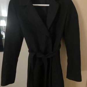 Svart kappa med bälte - Svart kappa i storlek S men mer som en xs. Klassisk design med knyt i midjan för en figursydd passform.