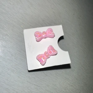 Rosa glittriga rosettörhängen - Söta rosa örhängen formade som rosetter med glittrig yta. Perfekta för att lägga till en lekfull touch till din outfit. De är små och lätta, vilket gör dem bekväma att bära hela dagen.