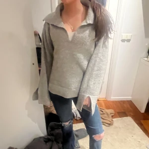 Grå stickad tröja med v-ringning - Säljer en mysig grå stickad tröja med v-ringning och långa ärmar. Perfekt för kyligare dagar och passar bra till jeans eller kjol. Tröjan har en avslappnad passform och är superbekväm att bära.