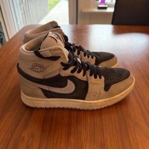 Nike Air Jordans i mocka och syntet - Snygga Nike Air Jordans i beige och svart med hög snörning. Skorna har en stilren design med Nike-logga på sidan och Zoom Air-märke på plösen. Perfekta för dig som vill ha en klassisk sneaker med modern touch.