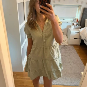 Grön klänning med knappar - Säljer en söt grön klänning med korta ärmar och knappar framtill. Perfekt för en sommardag. Klänningen har en luftig passform och volanger som ger en fin detalj.