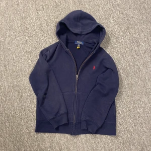 Mörkblå hoodie från Polo Ralph Lauren - Säljer en snygg mörkblå hoodie från Polo Ralph Lauren med dragkedja och huva i storlek m för barn (10-12)