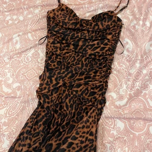 Leopardmönstrad klänning med smala axelband - Snygg leopardmönstrad klänning med smala axelband och rynkade detaljer. Perfekt för en djärv look!