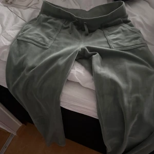 Gröna mjukisbyxor från Juicy Couture - Snygga gröna mjukisbyxor från Juicy Couture med bekväm passform. Byxorna har elastisk midja och praktiska fickor både fram och bak. Perfekta för en avslappnad stil. 