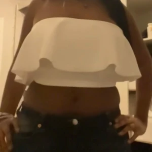 Vit axelbandslös topp - Snygg vit axelbandslös topp med volangdetalj. Perfekt för varma sommardagar eller en utekväll. Enkel och stilren design som passar till många olika outfits.