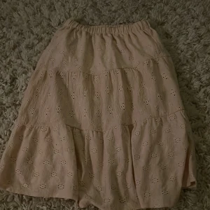  kjol från Zara - Säljer en söt beige kjol från Zara med broderade detaljer. Kjolen har en elastisk midja och är perfekt för varma dagar. Den har ett fint mönster som ger en romantisk känsla. Passar bra till både vardag och speciella tillfällen.