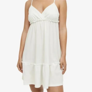  klänning - Säljer en söt vit klänning med smala axelband och volangdetaljer. Klänningen har en v-ringad design och är perfekt för varma dagar. Den är kort och luftig, vilket gör den idealisk för sommaren.💕💕